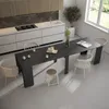 A modern kitchen and dining area with a large, dark wood extendable dining table set with white chairs and stools, in front of a sleek white kitchen counter with a gas stove and sink. Anteprima dell’immagine prodotto