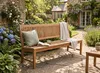 Massive Teakholzbank Kingsbury 180 cm in Natur, Gesamtansicht in sonnigem Garten mit Kissen und Decke. Produktbild-Vorschau