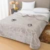A bed with a beige blanket, pillows, and a bedside table with flowers. Podgląd zdjęcia produktu