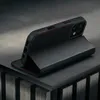 A black leather iPhone case with red stitching is displayed on a dark, textured surface. Voir les images du produit