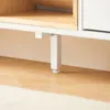 A close-up view of the leg and bottom of a white cabinet, resting on a wooden floor. Náhľad obrázku produktu