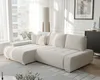 A modern living room with a beige sectional sofa, a floor lamp, and a window with sheer curtains. Produktbild-Vorschau