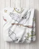 A close-up of a white fabric with a watercolor-style print of two snowy owls flying, carrying letters on broomsticks, surrounded by stars and magical rings. The fabric is draped, suggesting it could be a blanket or pillowcase. Produktbild-Vorschau