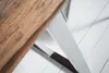 A close-up view of a wooden tabletop and a metal leg of a table, set against a white tiled floor. Produktbild-Vorschau