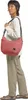 A person wearing a long-sleeved shirt and pants, carrying a red bag over their shoulder. Produktbild-Vorschau