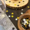 A close-up view of star-shaped confetti scattered on a dark wooden table, with a wooden bowl filled with more confetti in the foreground. Produktbild-Vorschau