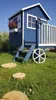 A blue wooden playhouse with white trim and a white railing, set in a grassy yard with a blue sky. Produktbild-Vorschau