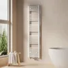 A white towel radiator is mounted on a light beige wall in a bathroom, next to a large window and a white bathtub. Náhľad obrázku produktu