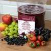 A product packaging for wine yeast with fruit ingredients surrounding it, and a large container of red liquid in the background. Produktbild-Vorschau