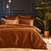 A bedroom scene with a bed dressed in rust-colored velvet bedding, a large potted plant, and decorative pendant lights. Anteprima dell’immagine prodotto