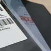 A close-up view of a smartphone screen protector with text and a barcode on a label in the foreground, and a black background. Produktbild-Vorschau