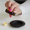 A hand is shown dripping liquid from a small brown bottle into a black dish. Náhled obrázku produktu