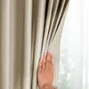 A hand is pulling back a beige curtain, revealing a sheer white curtain behind it. Produktbild-Vorschau