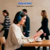 A woman wearing headphones is reading a book at a table, with other people blurred in the background. Produktbild-Vorschau