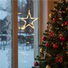 A Christmas tree decorated with ornaments and lights, viewed through a window with a star-shaped light hanging on it. Outside the window, it appears to be snowing with blurred lights in the distance. Produktbild-Vorschau