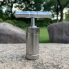 A metal pollen press sits on a rock outdoors, with trees and grass in the background. Produktbild-Vorschau