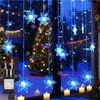 A window decorated with blue snowflake string lights, with a Christmas tree and candles visible in the background. Anteprima dell’immagine prodotto