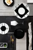 A flat lay arrangement of black and white plates, a wine glass, cutlery, and a decorative stone. Produktbild-Vorschau