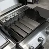 A close-up view of the interior of a stainless steel grill, showing the flavorizer bars and a decorative metal plate. Podgląd zdjęcia produktu