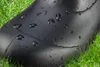 A close-up of a black rubber boot with water droplets on it, resting in green grass. Produktbild-Vorschau