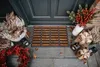 A doormat with holiday decorations and gifts placed around it in front of a dark gray door. Produktbild-Vorschau