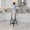 A woman is cleaning a kitchen range hood while standing on a step stool. Voir les images du produit