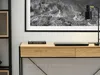 A modern desk with a laptop and a book on it, placed against a wall with a large framed picture above it. Náhled obrázku produktu