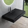 A modern black matte washbasin mounted on a wall, with a chrome faucet. The background shows a large circular mirror reflecting a green lawn and a window with a view of trees and grass. Produktbild-Vorschau