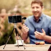 A man is sitting at a table outdoors, talking to a smartphone mounted on a tripod with a microphone attached. Podgląd zdjęcia produktu
