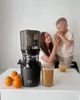 A woman and child are next to a juicer with oranges and juice on a table. Produktbild-Vorschau