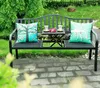 A black metal garden bench with two decorative pillows and a small table with two cups and flowers, set on a brick patio surrounded by greenery. Produktbild-Vorschau