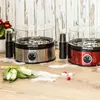 Two egg cookers are shown on a wooden surface with some tulips and feathers. Produktbild-Vorschau
