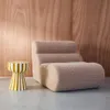 A fluffy beige armchair and a striped side table are placed in front of a wooden paneled wall. Produktbild-Vorschau
