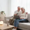 An older couple sitting on a couch, using a laptop and a credit card. Podgląd zdjęcia produktu