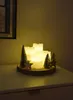 A decorative arrangement of LED candles and miniature Christmas trees on a wooden base, placed on a white surface. Produktbild-Vorschau