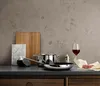 A kitchen counter with cooking utensils, a cutting board, a glass of red wine, and a piece of meat. Náhľad obrázku produktu