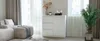 A modern living room with a white kommode, a sectional sofa, and a potted plant. Produktbild-Vorschau