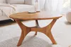 A wooden coffee table is placed on a rug in a living room setting, with a sofa and candles visible. Produktbild-Vorschau