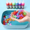 Hände halten bunte Gel-Figuren in einem blauen Tablett, mit sechs Flaschen farbigem Gel im Hintergrund Produktbild-Vorschau