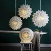 Several white paper star lanterns are displayed in a room with dark green walls. One lantern is placed on a white stool on a table, while three others hang from the ceiling. Podgląd zdjęcia produktu