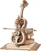 A 3D mechanical wooden model of a cello with intricate gears and decorative elements, resting on a stack of books. Náhľad obrázku produktu