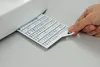 A hand is holding a stitch chart that is partially inserted into a sewing machine. Produktbild-Vorschau