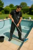 A man is cleaning an empty swimming pool with a broom. Produktbild-Vorschau