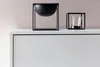 Two black decorative objects are placed on top of a white cabinet against a light pink wall. Náhled obrázku produktu