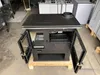 A black wood-burning stove with its doors open, displayed in a warehouse or storage area. Produktbild-Vorschau