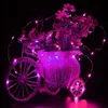 A decorative bicycle-shaped basket filled with artificial flowers, illuminated by pink LED string lights. Voir les images du produit