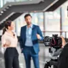 A man and a woman are being filmed by a camera operator in a modern office building. Náhled obrázku produktu