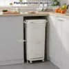 A beige kitchen trash can with a liner is shown next to kitchen cabinets. There is a measurement line indicating its height. Anteprima dell’immagine prodotto