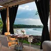 Outdoor dining area with a view of a beach and ocean, featuring black curtains. Náhľad obrázku produktu