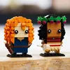 Two Lego BrickHeadz figures, one resembling Merida from Brave and the other Vaiana from Moana, are displayed on a wooden surface. Produktbild-Vorschau